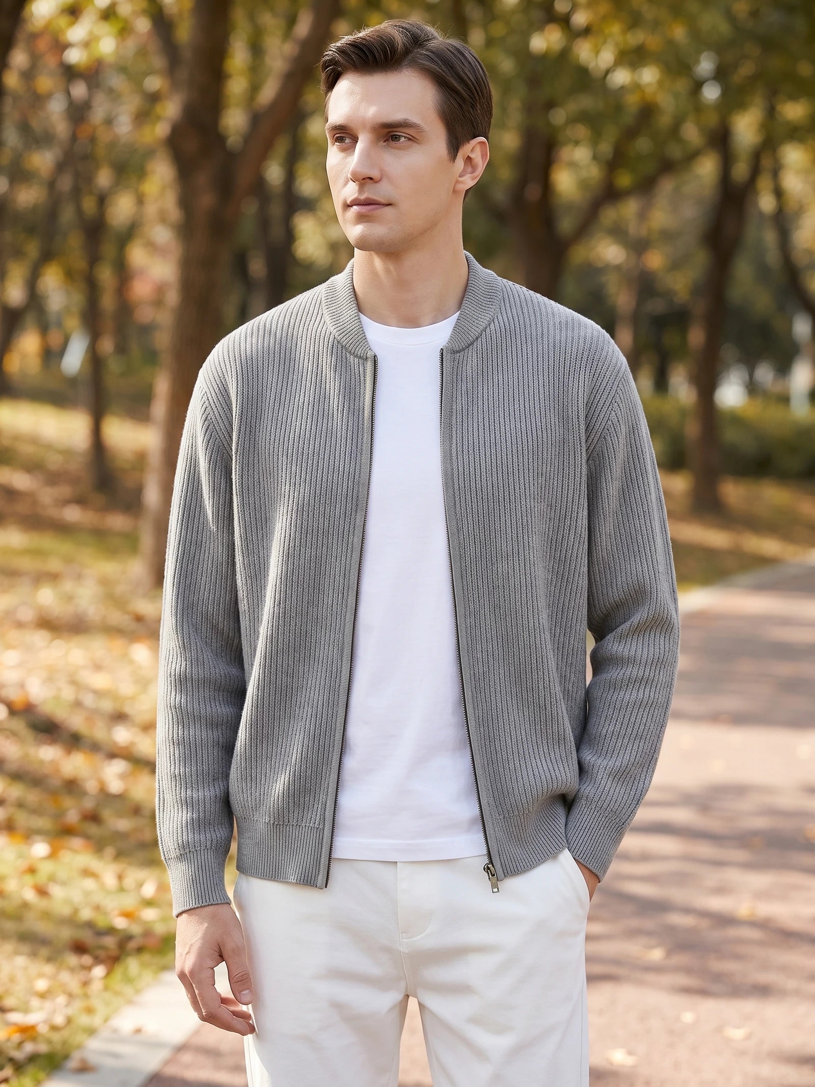 Man wearing a Gray ribbed zip up cardigan with a stand collar while walking along a tree-lined path.