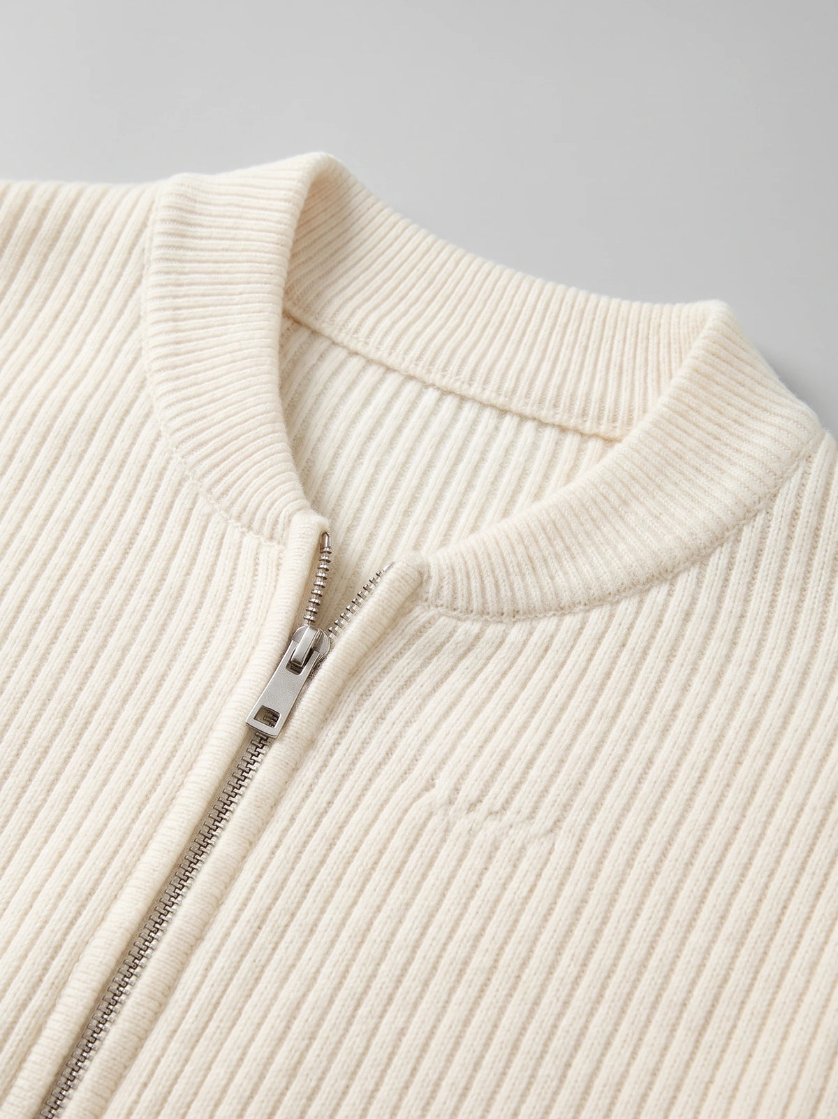 Close-up of the White zip up cardigan showing its ribbed knit stand collar and metal front zipper.